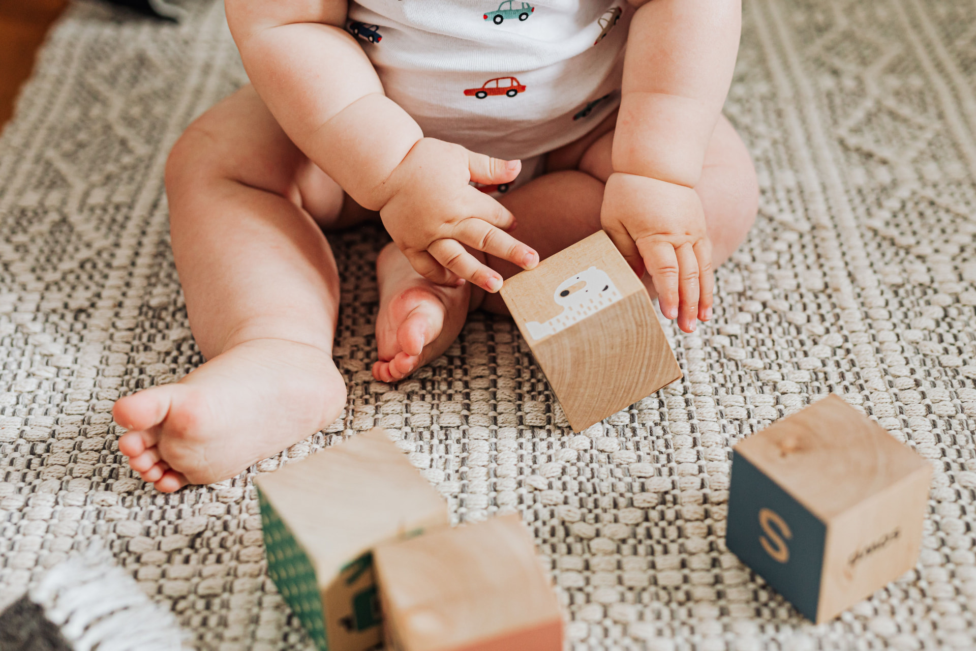 Baby sitting on a textured rug playing with wooden alphabet blocks